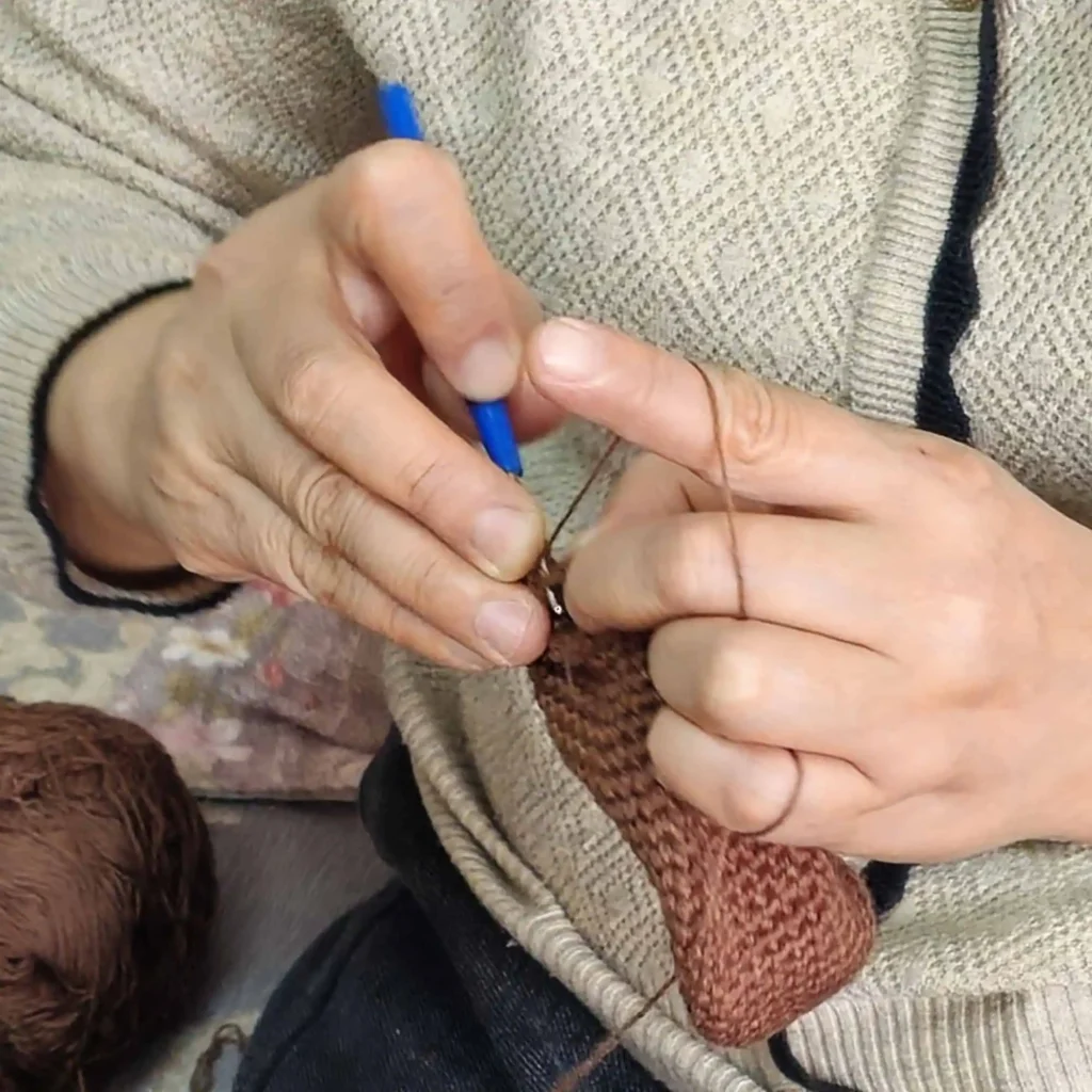 Nahaufnahme: zwei Hände beim Häkeln mit Häkelnadel; der Garnfaden wird durch die Finger geführt.