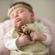 Sleeping baby holding the monkey ring rattle with crocheted yarn and beechwood ring from above