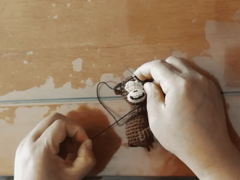 Close‑up: hands embroidering the eye onto a crocheted figure.
