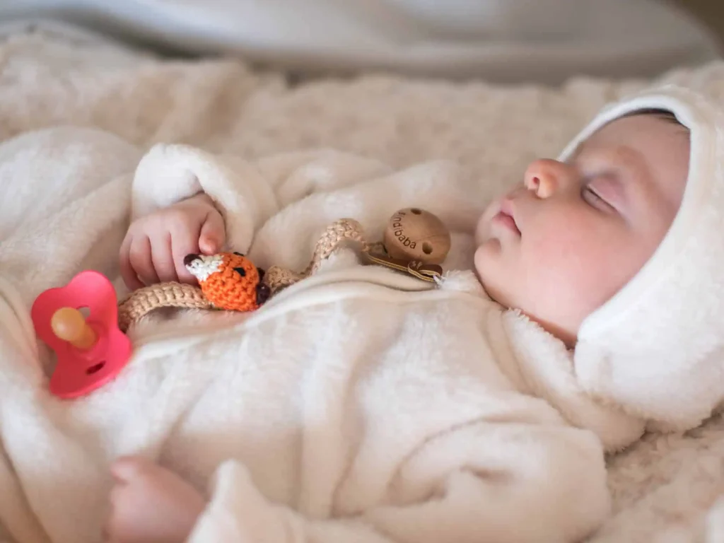 Schlafendes Baby mit Schnullerkette im Fuchs-Design und befestigtem Schnuller.