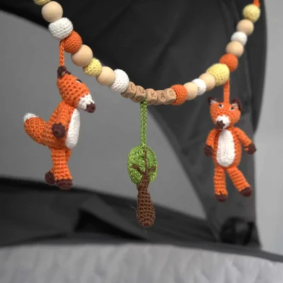 Personalisierte Kinderwagenkette mit Fuchs-Motiv und Namen Lukas am Kinderwagen befestigt.