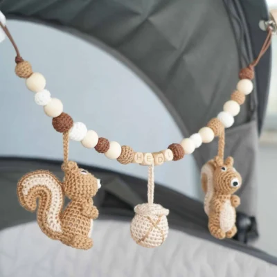 Personalisierte Kinderwagenkette mit Eichhörnchen-Motiv und Namen Hedi am Kinderwagen befestigt.