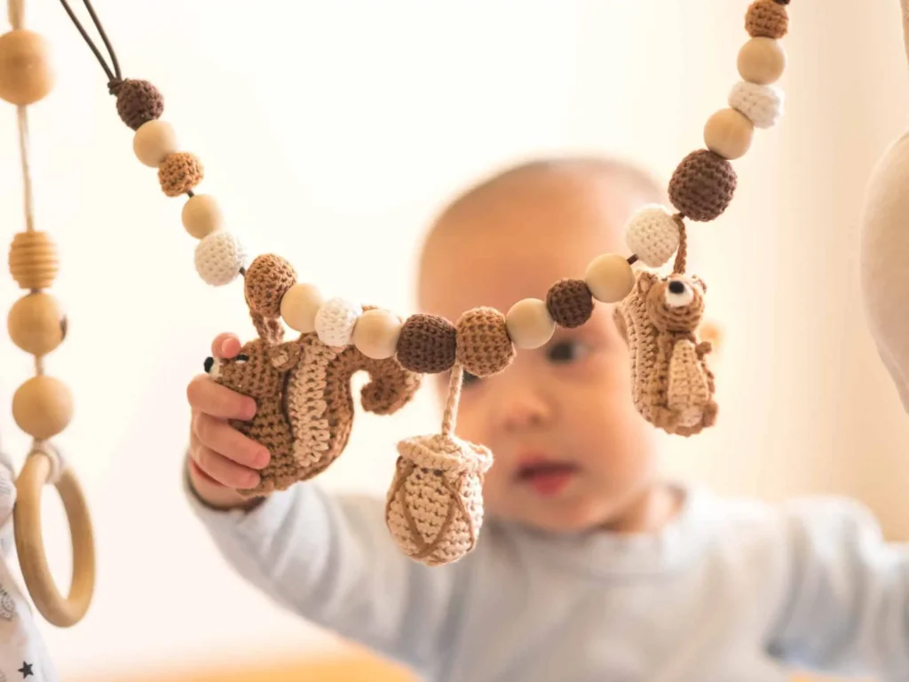 Baby greift nach einer Kinderwagenkette mit Eichhörnchen-Motiv am Spielbogen.