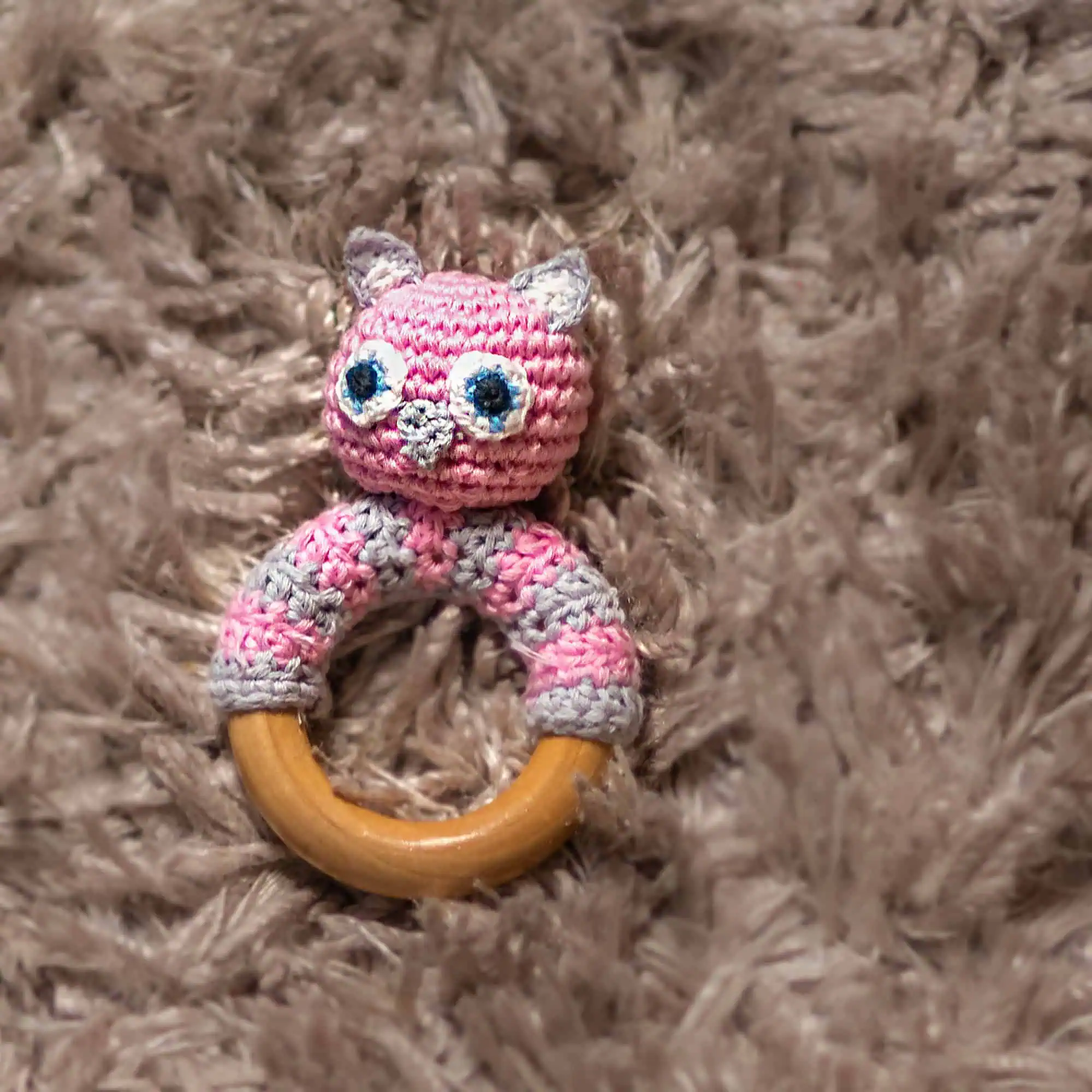 Owl LUNA rattle ring arranged on a plush surface in warm color tones