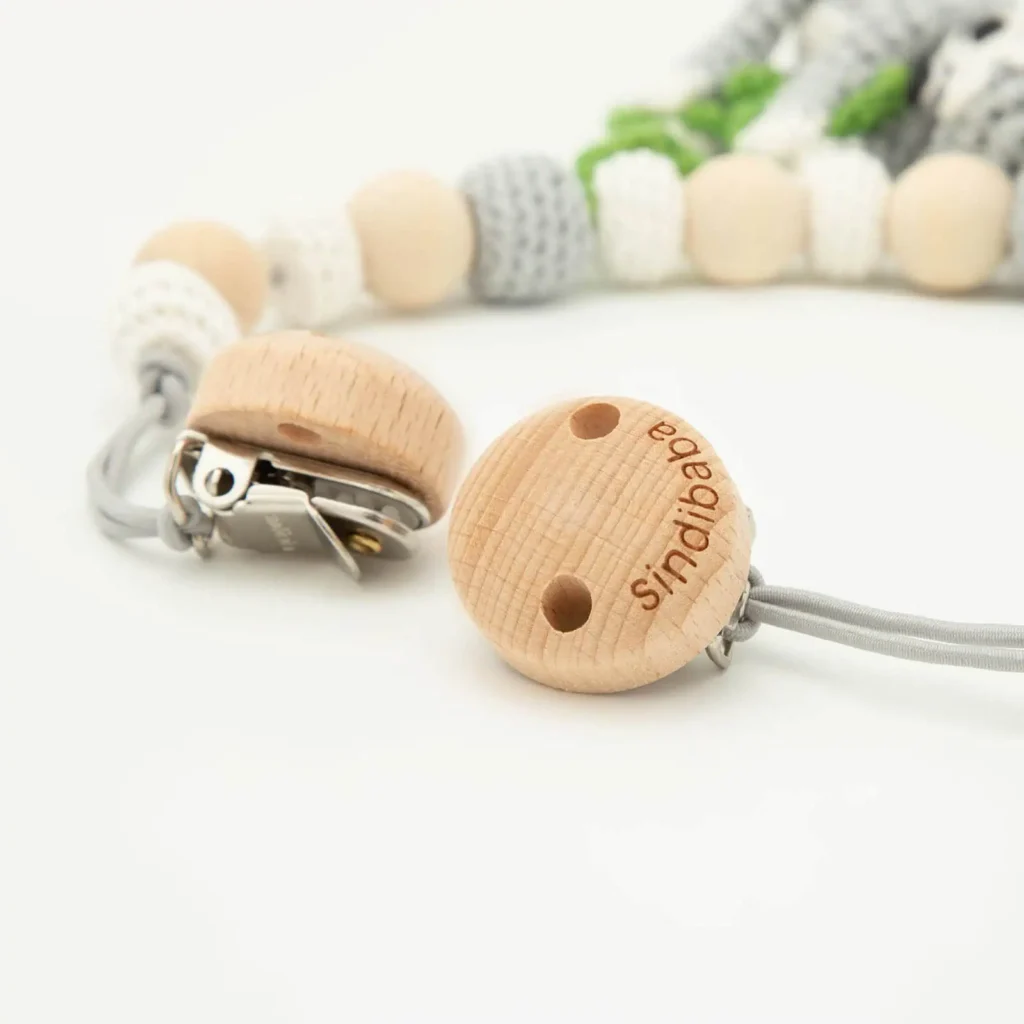 Close-up of the wooden clips on a stroller chain with sloth motif, visible wood grain and metal clamp, beads softly blurred in the background