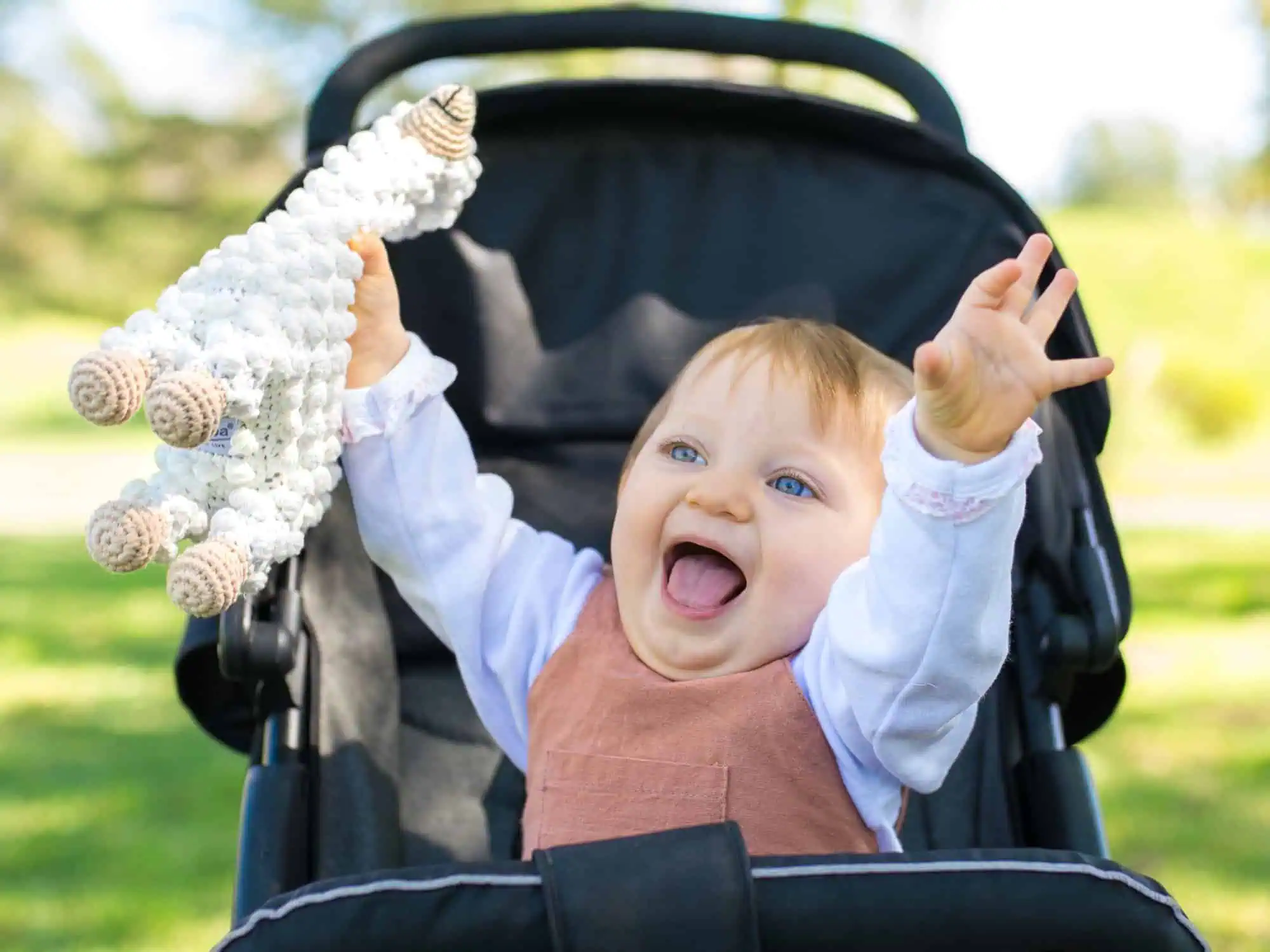 Cheerful toddler in a stroller holding a SindiBaba llama cuddle toy in the park.