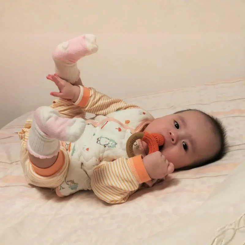 Rattle Ring Fox FRED – Baby Use Scene Full View Baby lying on its back with raised legs holding the Fox FRED rattle ring in one hand