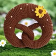Crochet baby rattle pretzel with sunflower on colored background