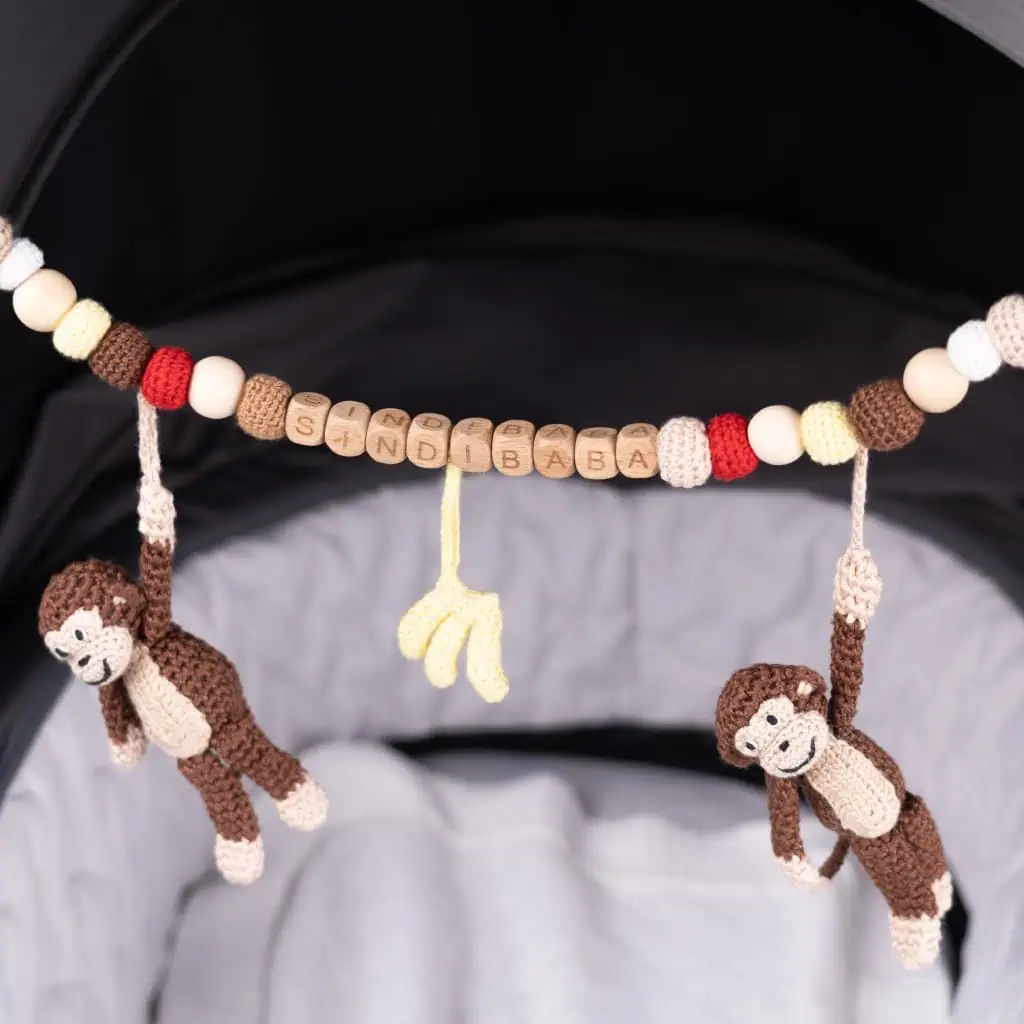 Personalized stroller chain monkey Charlie in brown with brand name SINDIBABA – hand‑crocheted baby toy on a stroller, detailed view with wooden clips and natural materials
