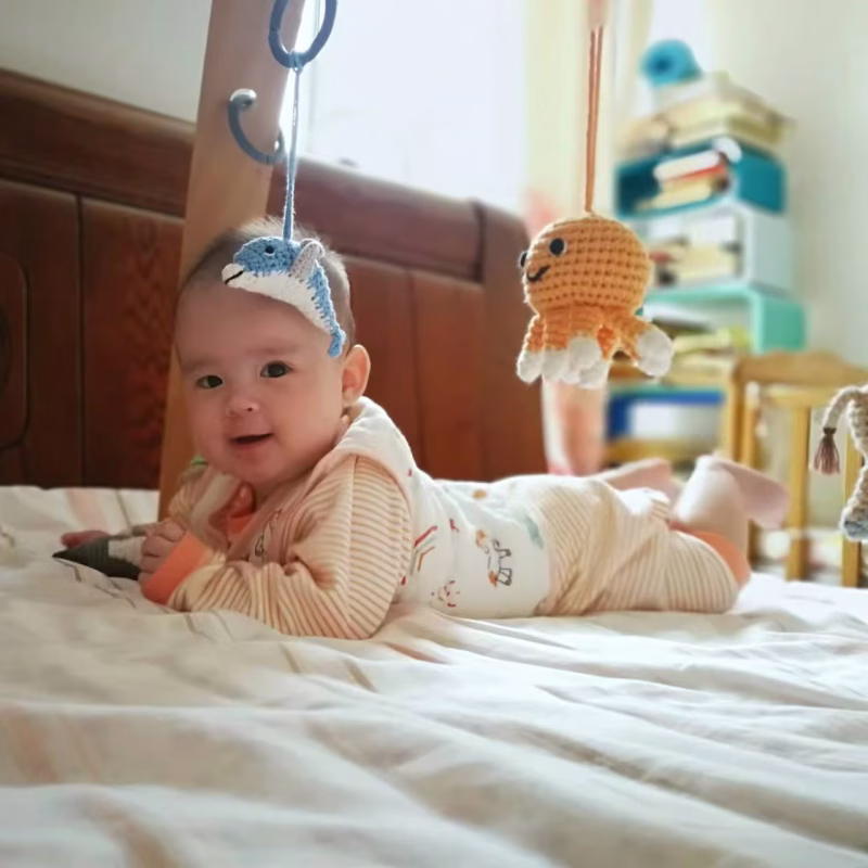 12529-baby-mobile-sea-animals-lifestyle-crib-bokeh Gehäkelte Krake und Delfin als Hängefiguren an einem Spielbogen, aufgenommen auf Augenhöhe eines im Bett liegenden Babys.