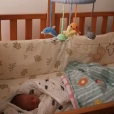 Gehäkeltes Baby-Mobile MEERESTIERE aus der Vogelperspektive über einem schlafenden Baby im abgedunkelten Gitterbett.