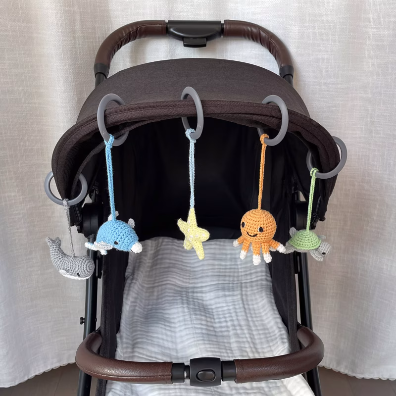 12529-baby-mobile-sea-animals-lifestyle-stroller Praxisanwendung der die fünf abnehmbaren gehäkelten Meerestier-Figuren, befestigt mit Ringen nebeneinander an einem Kinderwagen-Sonnenverdeck