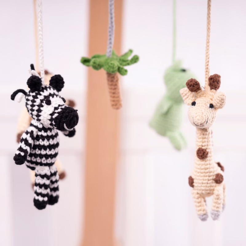12540-baby-mobile-safari-2-closeup-details Nahaufnahme der am Mobile hängenden gehäkelten Tierfiguren mit Fokus auf Zebra und Giraffe vor weichgezeichnetem Hintergrund