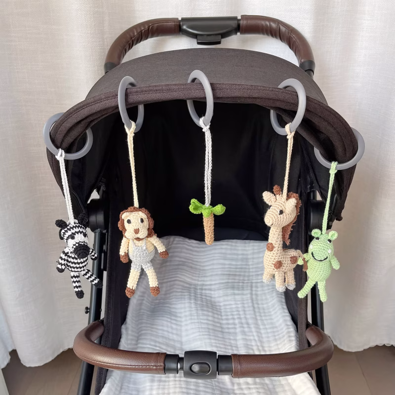 12540-baby-mobile-safari-2-lifestyle-stroller Praxisanwendung der fünf abnehmbaren gehäkelten Savannentiere, befestigt mit Ringen nebeneinander an einem Kinderwagen-Sonnenverdeck