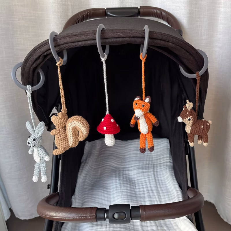 12541-baby-mobile-forest-animals-1-lifestyle-stroller Praxisanwendung der fünf abnehmbaren gehäkelten Waldtier-Figuren, befestigt mit Ringen nebeneinander an einem Kinderwagen-Sonnenverdeck