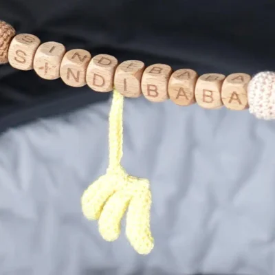Close‑up of a personalized stroller chain with desired name and hanging banana elements.