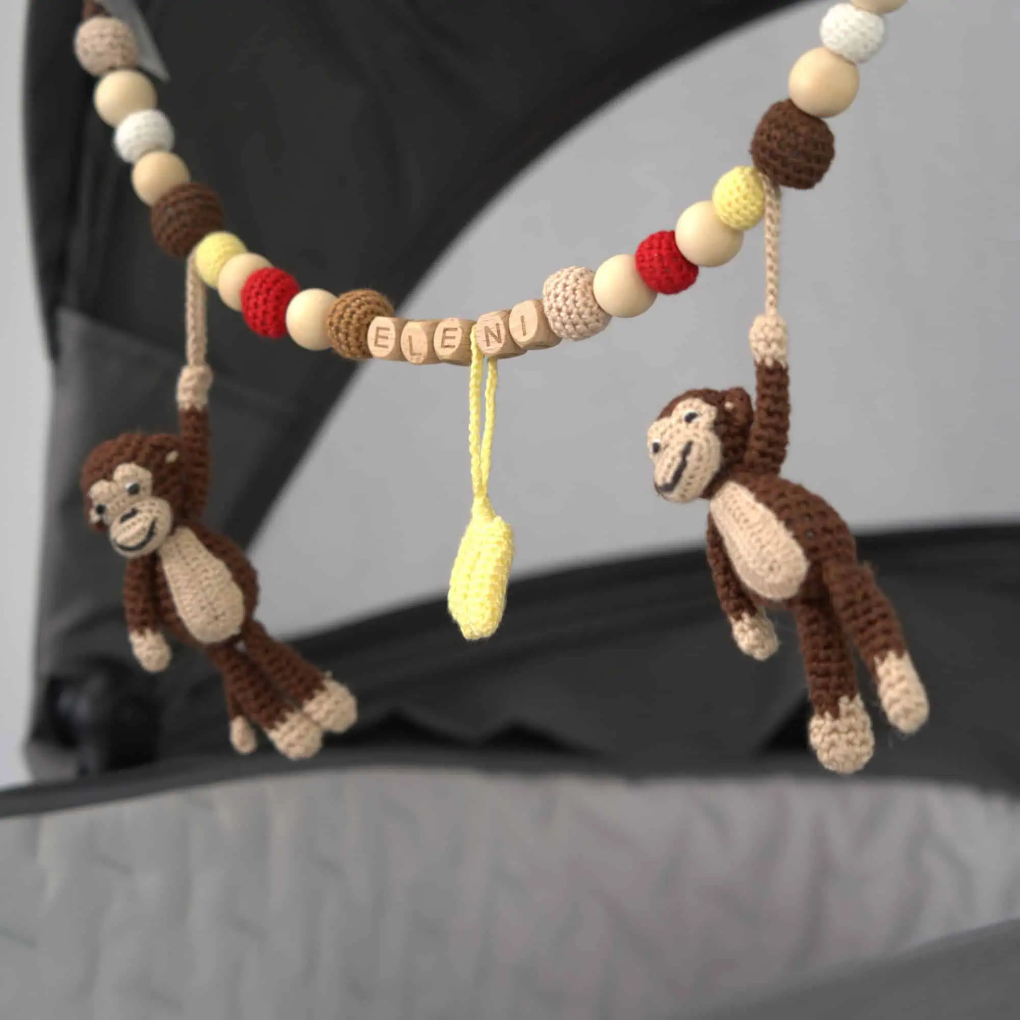 Personalisierte Kinderwagenkette mit Affe-Motiv und Namen Eleni am Kinderwagen befestigt.