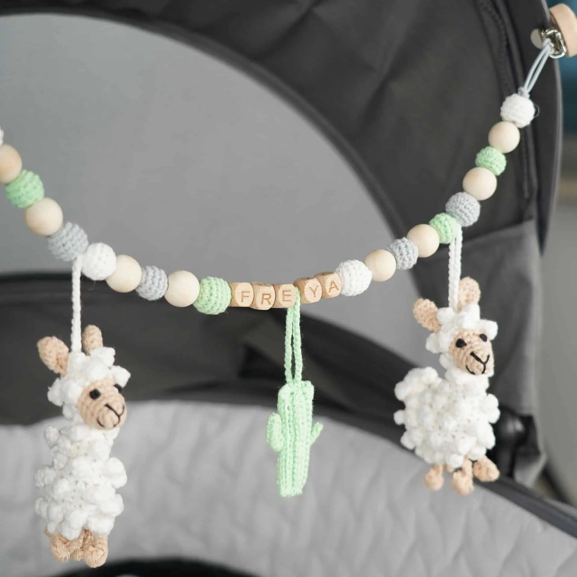 Personalisierte Kinderwagenkette mit Lama-Motiv und Namen Freya am Kinderwagen befestigt.