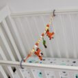 Sehr helle Lifestyle-Aufnahme der elastischen Fuchs FRED Kinderwagenkette, die mittels grauen Ringen über die volle Länge eines weißen Babybettes gespannt ist.