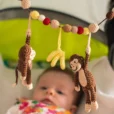 Lifestyle shot from a higher angle from the top right into the light green stroller with beige lining; the focus is clearly on the crocheted hanging figures.