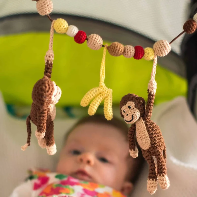 12625-stroller-chain-monkey-charlie-lifestyle-stroller-high-angle-view Lifestyle shot from a higher angle from the top right into the light green stroller with beige lining; the focus is clearly on the crocheted hanging figures.